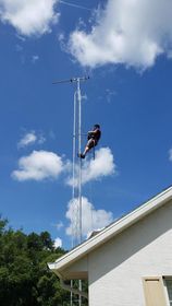 A man is climbing a very tall antenna on top of a house.