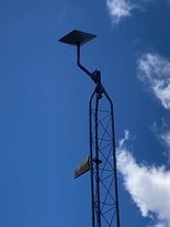 Tall metal tower with aStarlink dish tagainst a blue sky and clouds
