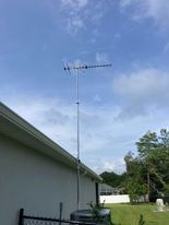 An antenna is sitting on top of a pole in front of a house.