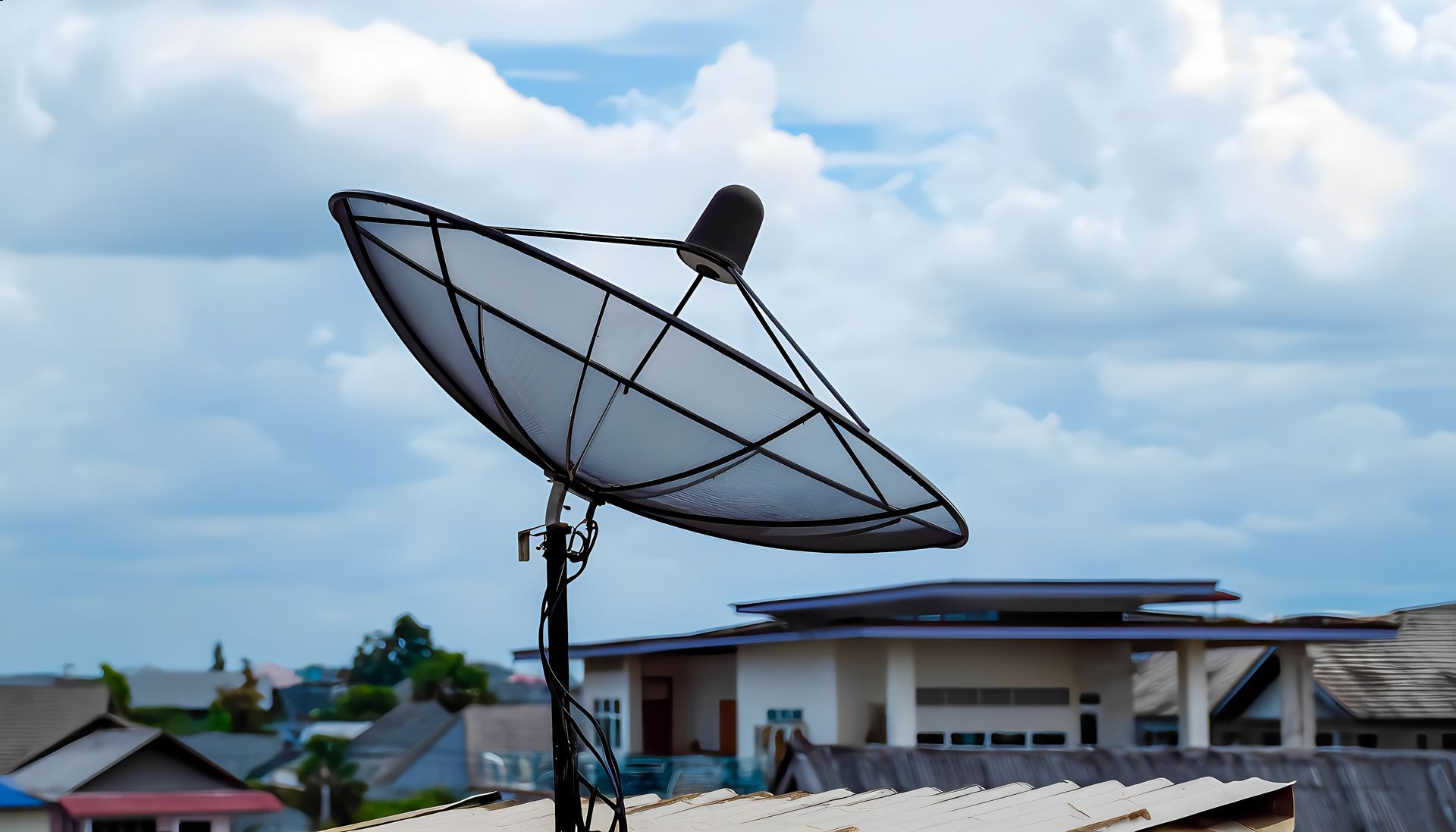 Satellite dish on a rooftop, with a cloudy sky background and nearby buildings.