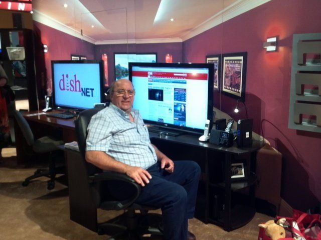 A man sits in a chair in front of a tv screen that says dishnet