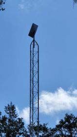 Tall metal tower with a Starlink dish  on top against a blue sky, above trees