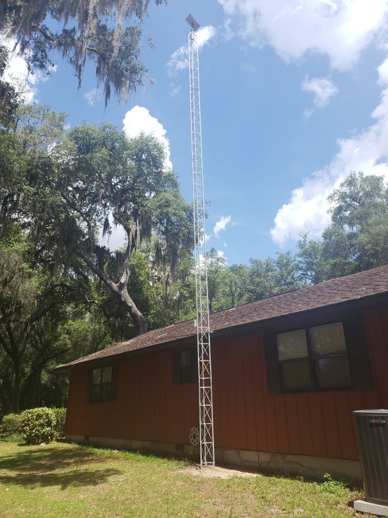 Wooden building with a tall metal antenna tower in a sunny, tree-lined yard