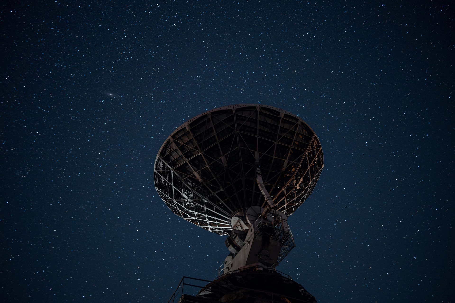 A large satellite dish is against a starry night sky.