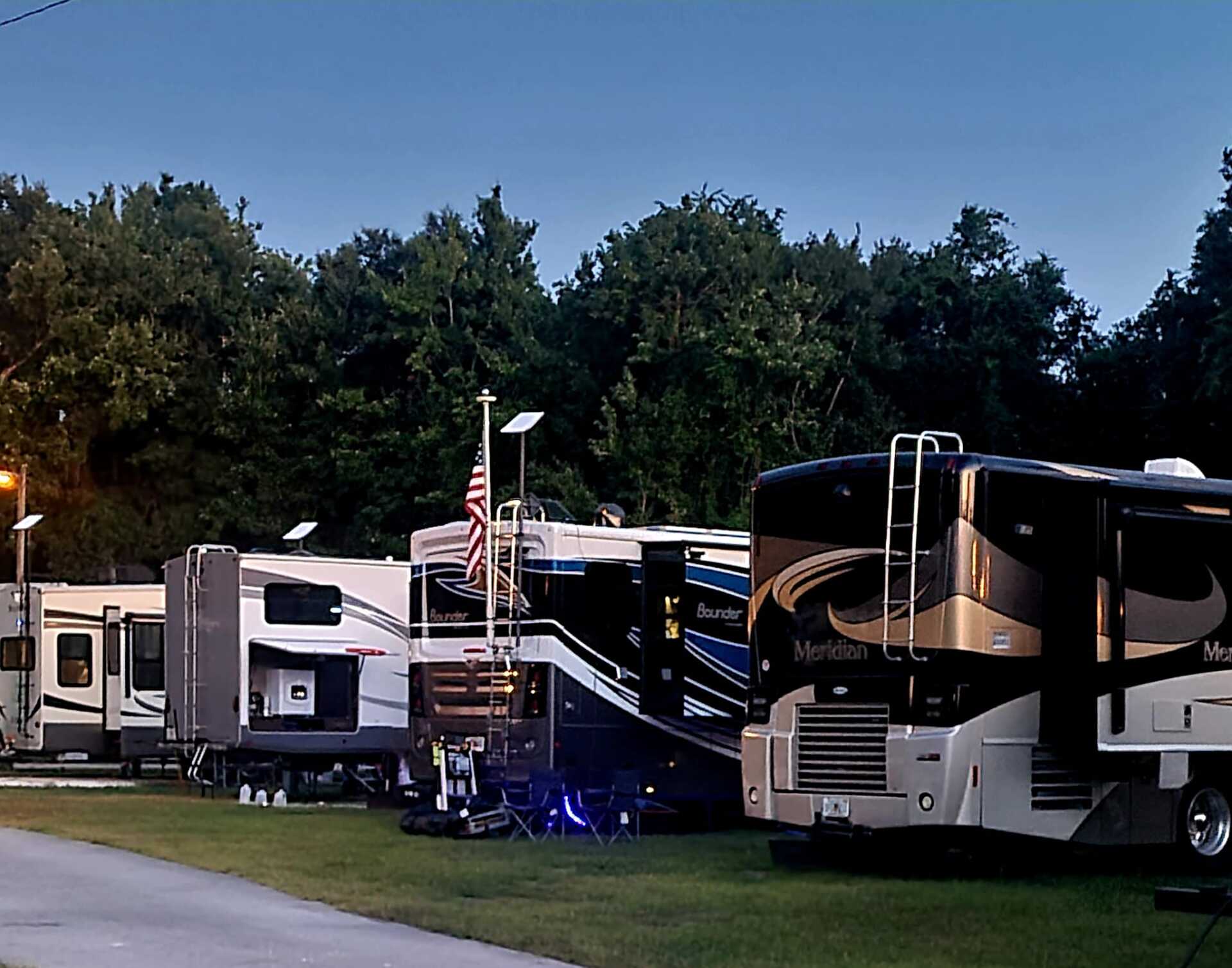 A row of rv 's are parked in a grassy area with trees in the background