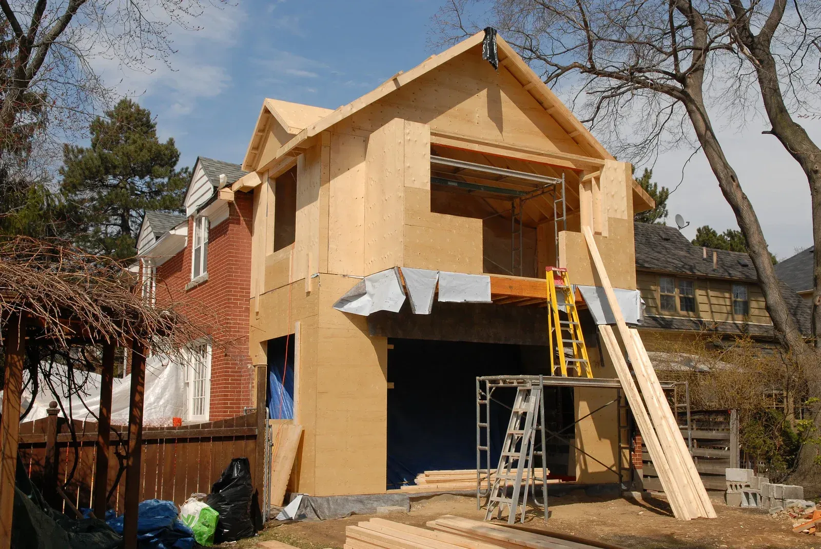 House exterior under renovation with plywood siding, ladders, and scaffolding
