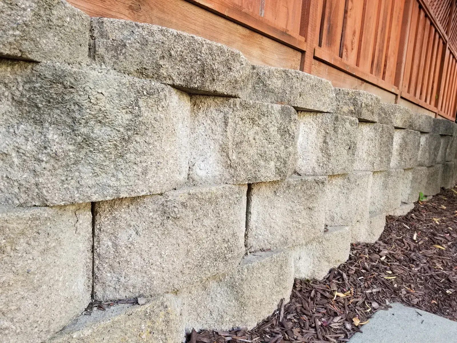 Stone retaining wall beneath a wooden fence, beside a mulch-covered garden bed