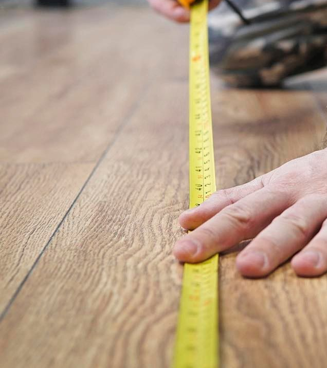 Hands measuring a wooden surface with a yellow tape measure
