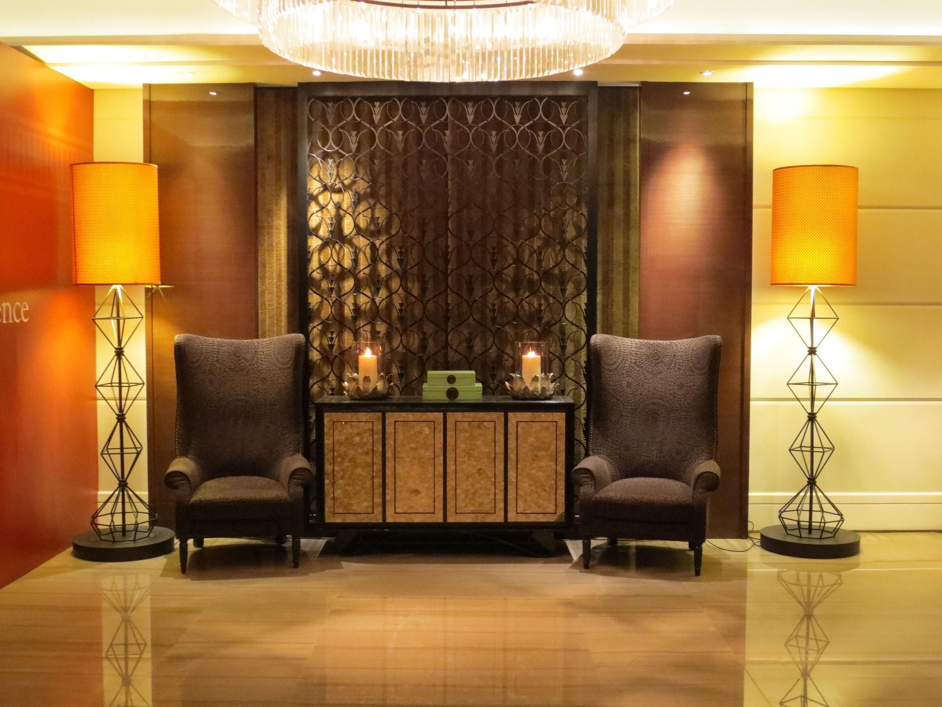 Elegant hotel lobby with two armchairs, a decorative cabinet, and warm amber lamps under a chandelier