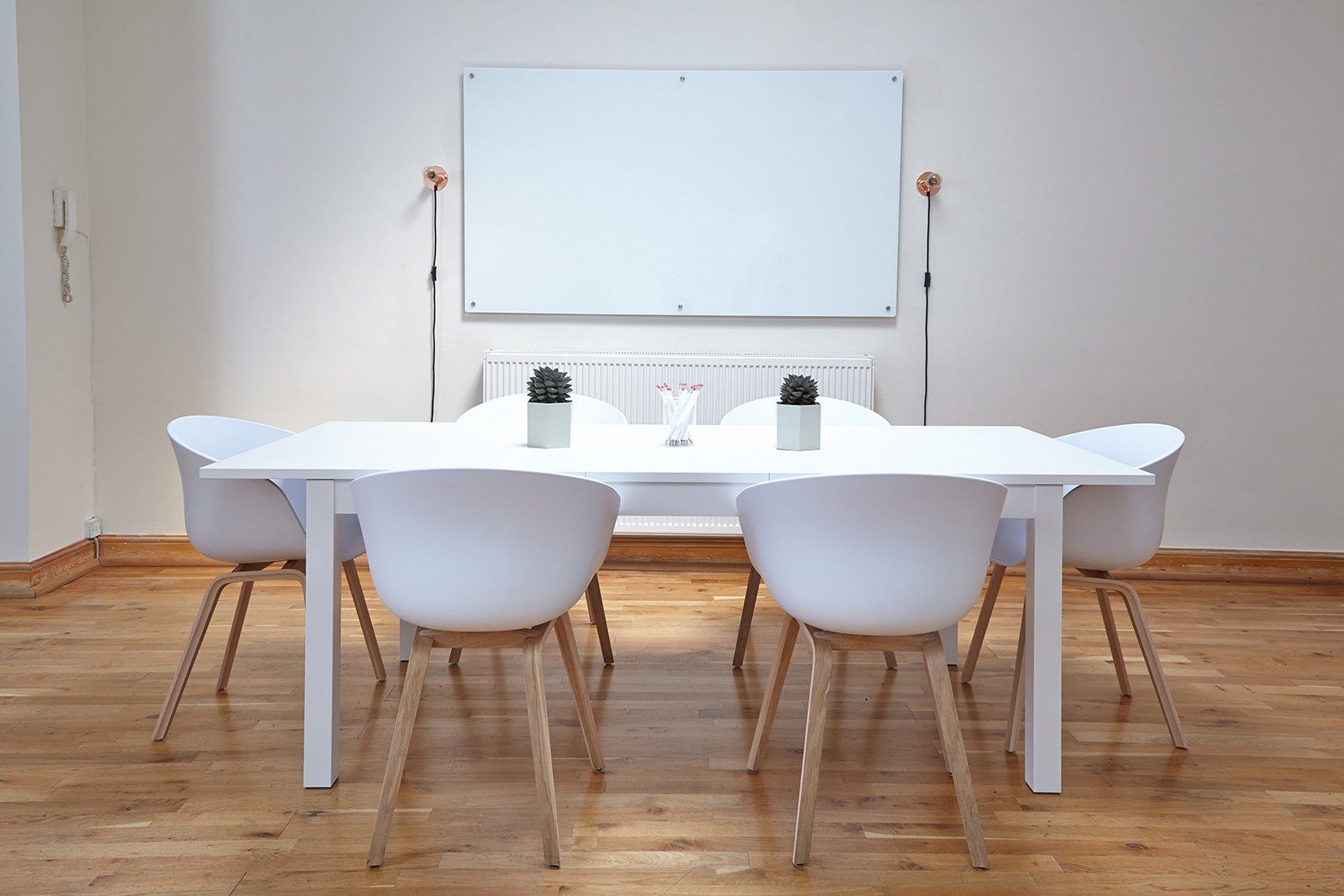 Minimal dining room with white table, chairs, and blank whiteboard against a wooden floor