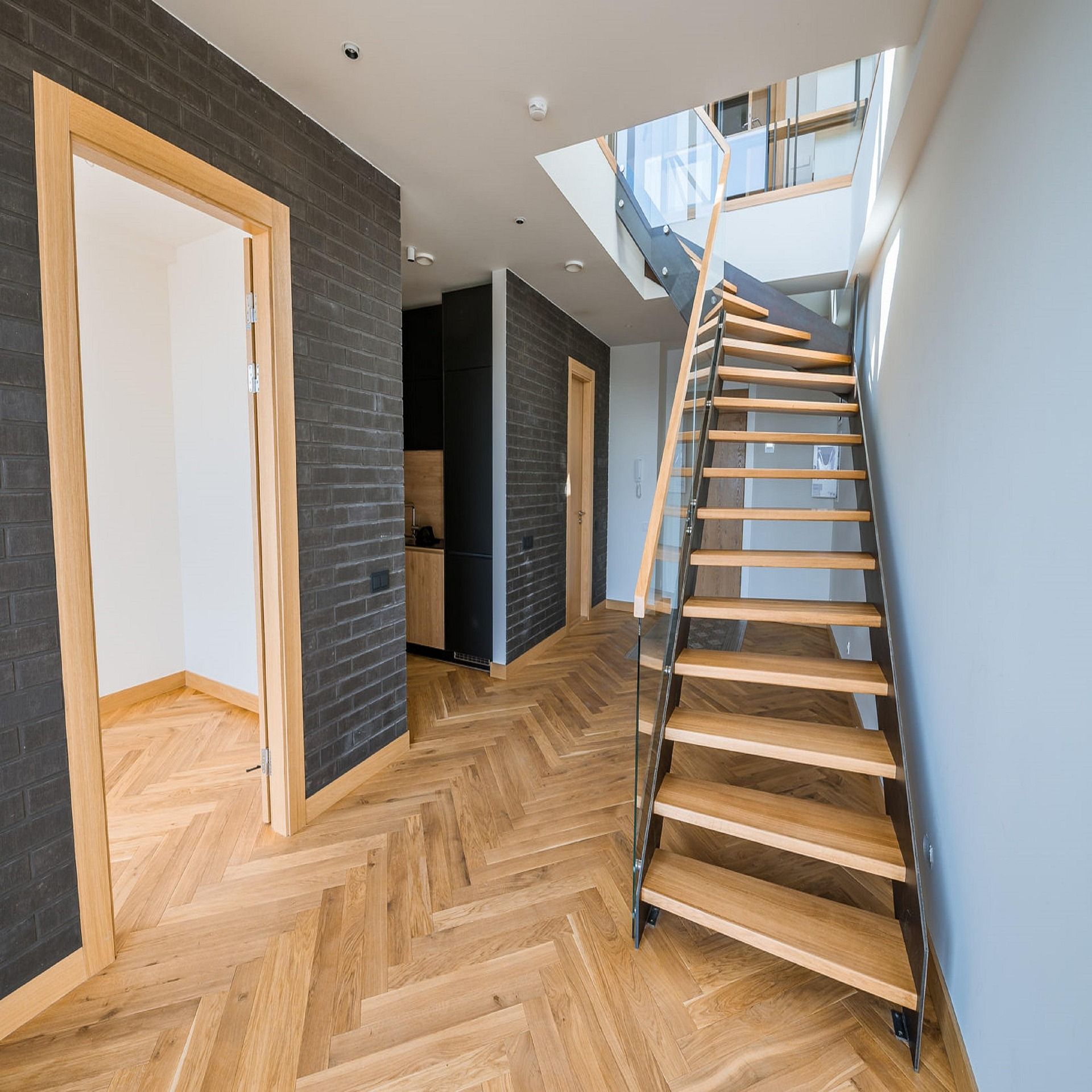 Modern hallway with herringbone wood floor, dark brick accent wall, and open staircase under skylight