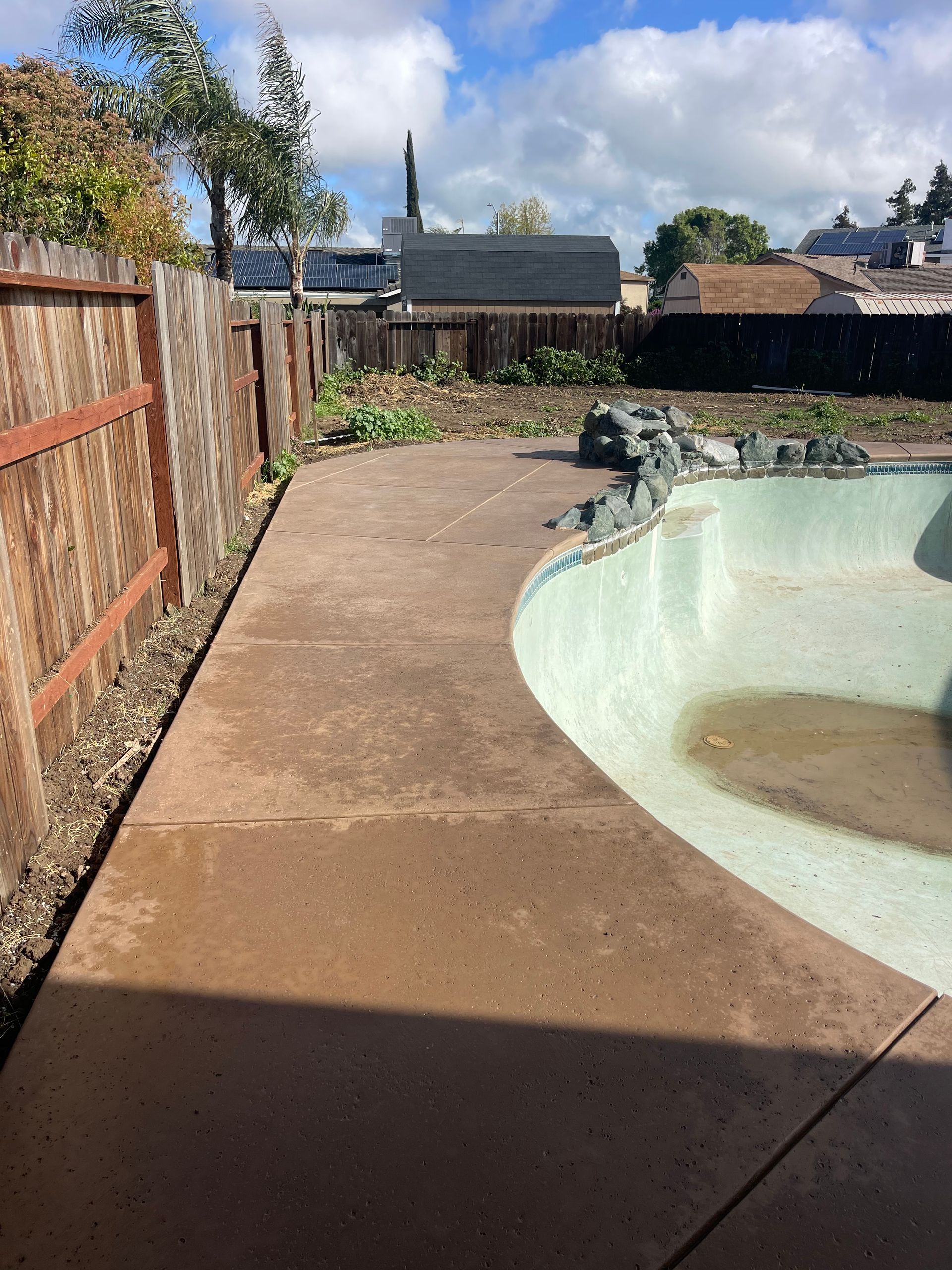 A concrete walkway leading to a swimming pool with a wooden fence in the background.