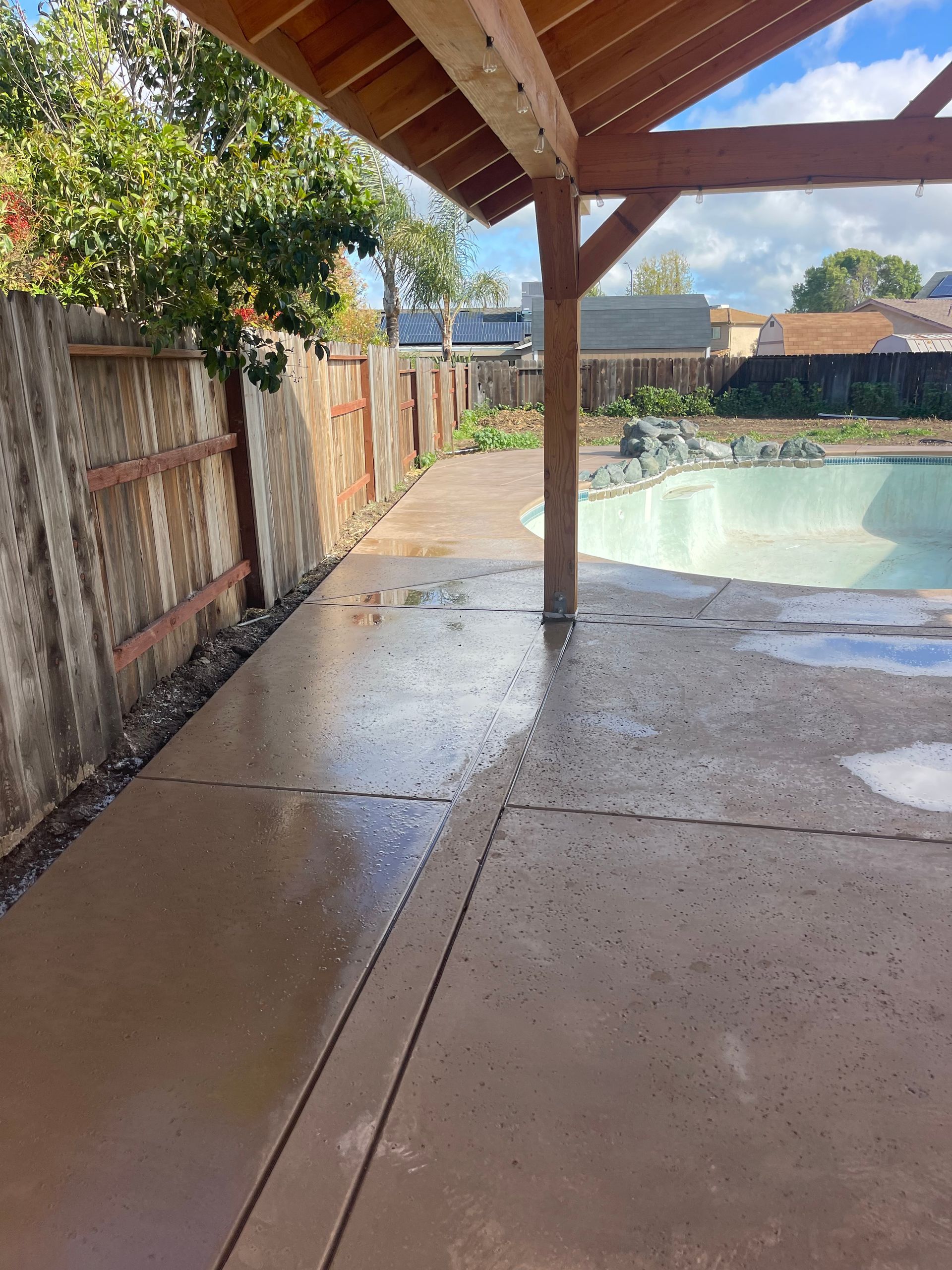 A patio with a wooden roof and a pool in the background.