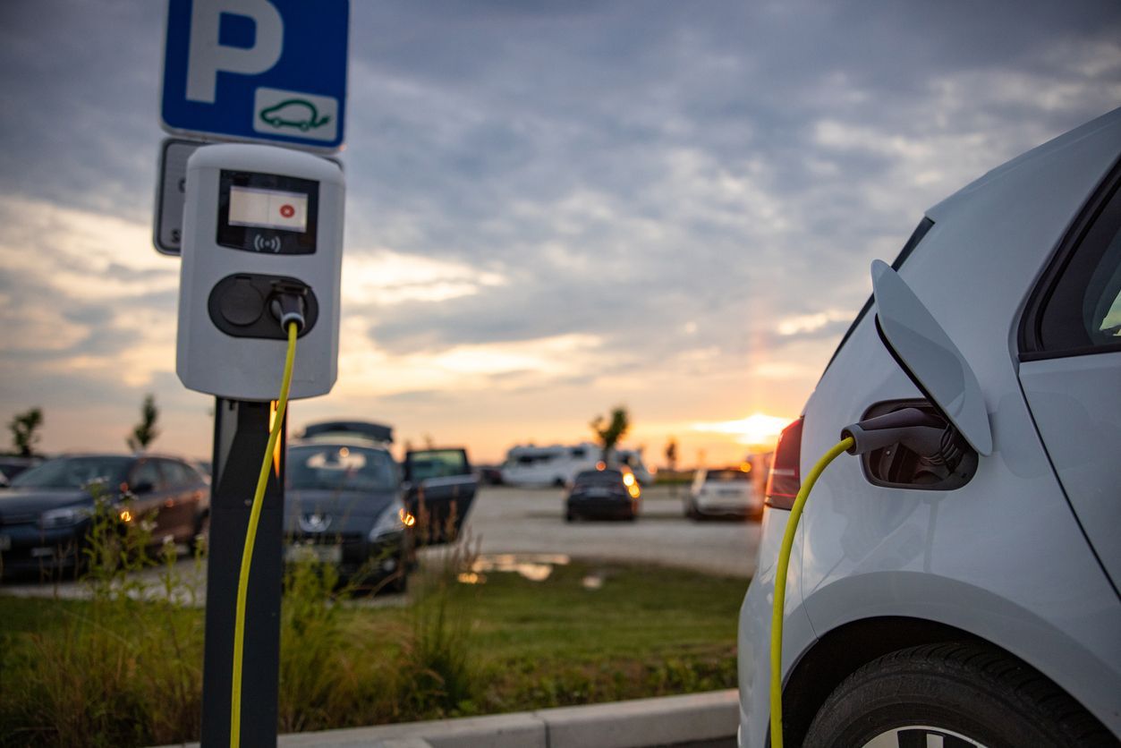 An electric car is being charged at a charging station in a parking lot.