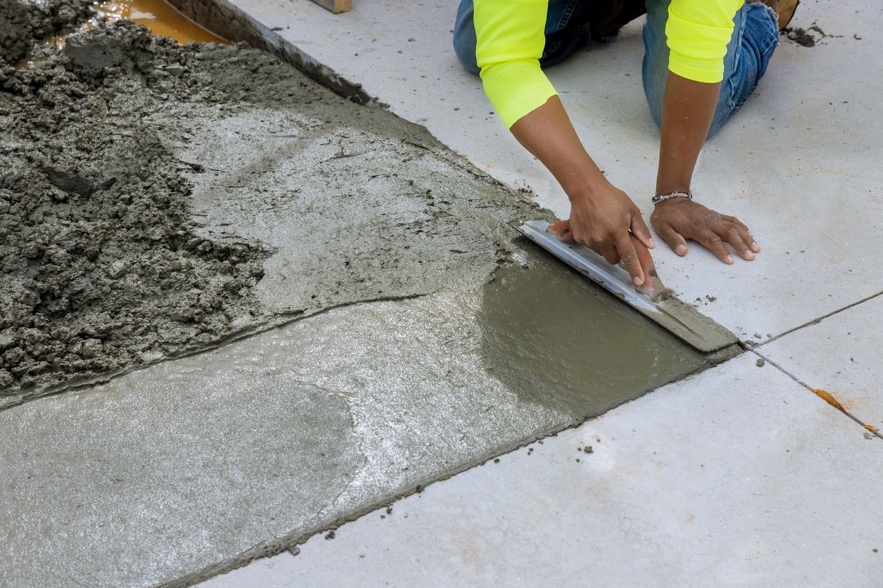 A person is laying concrete on the ground with a trowel.