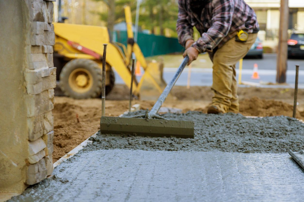 A man is spreading concrete on a sidewalk with a rake.