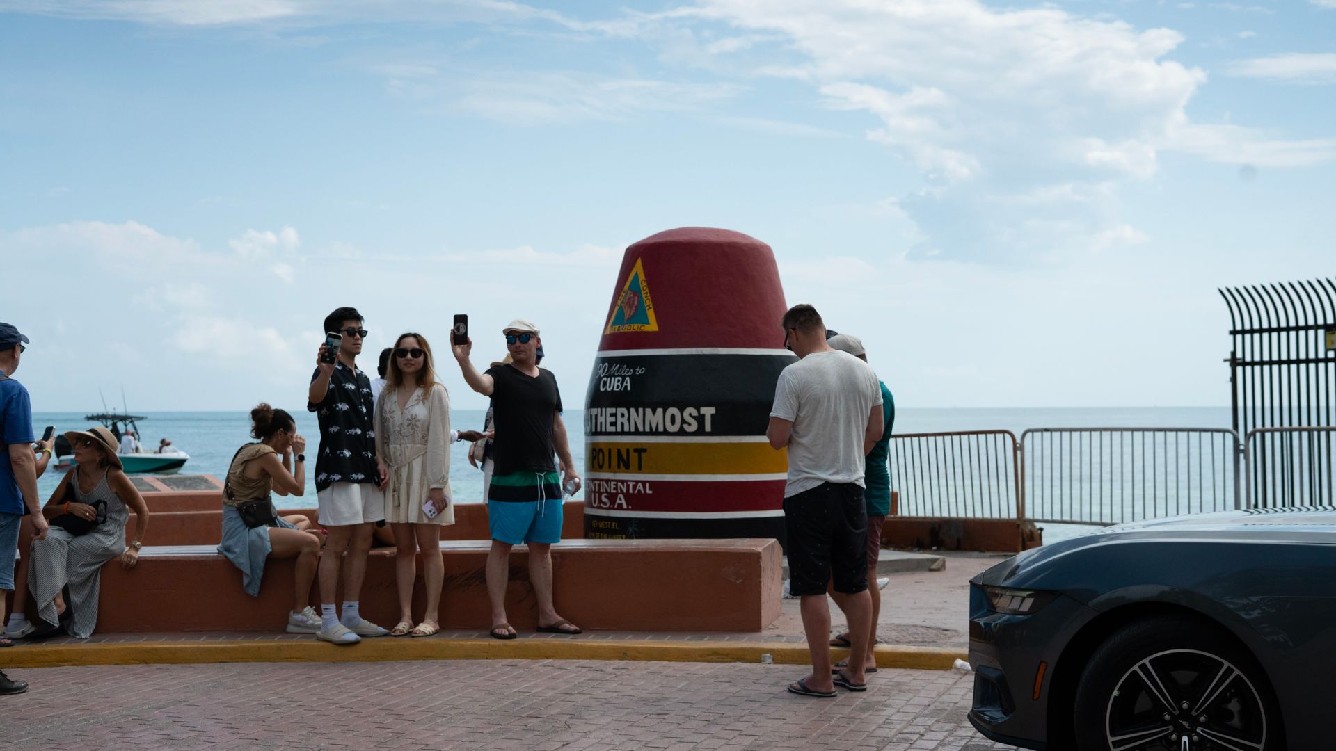Tourists taking photos at the Southernmost Point Buoy landmark in Key West, Florida, with the ocean in the background