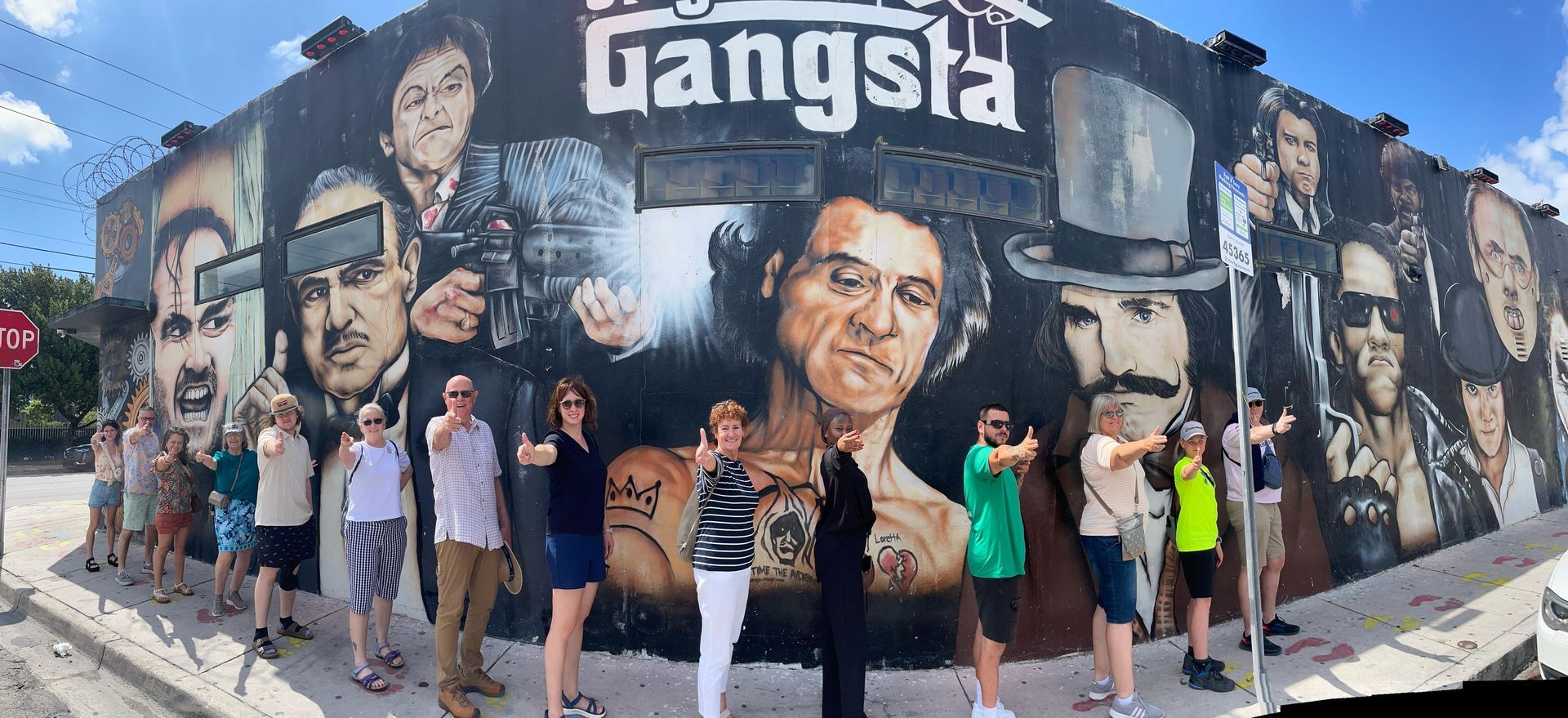 Tour group posing playfully with finger guns in front of the famous Gangster Legends mural in Wynwood during the Miami Private City Tour.