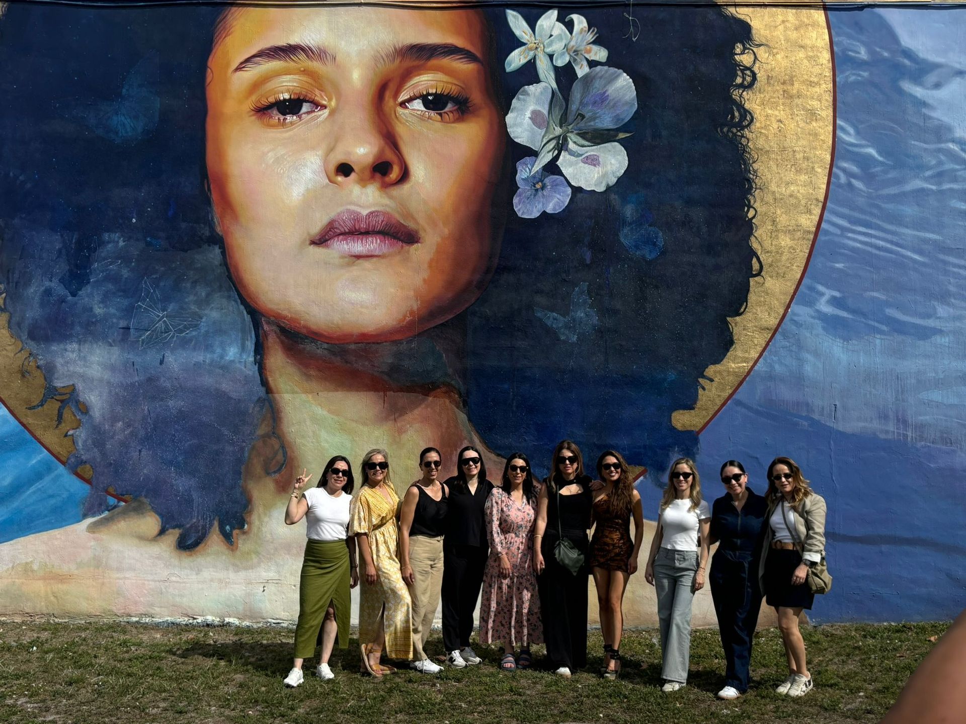 Group of women posing in front of a large, colorful mural of a woman's face with flowers in her hair in Wynwood during the Miami Private City Tour.