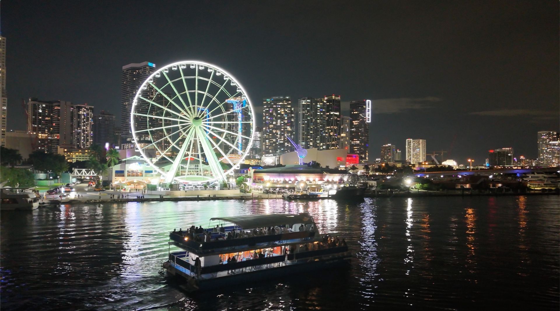Miami night tour sightseeing boat cruise passing Bayside Marketplace with the Miami skyline illuminated at night.
