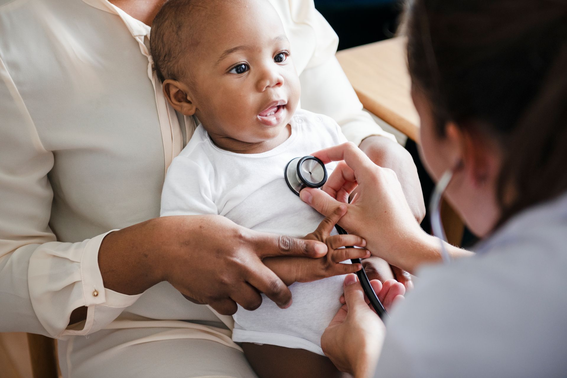 Doctor checking a baby’s heartbeat with a stethoscope while a caregiver holds the child