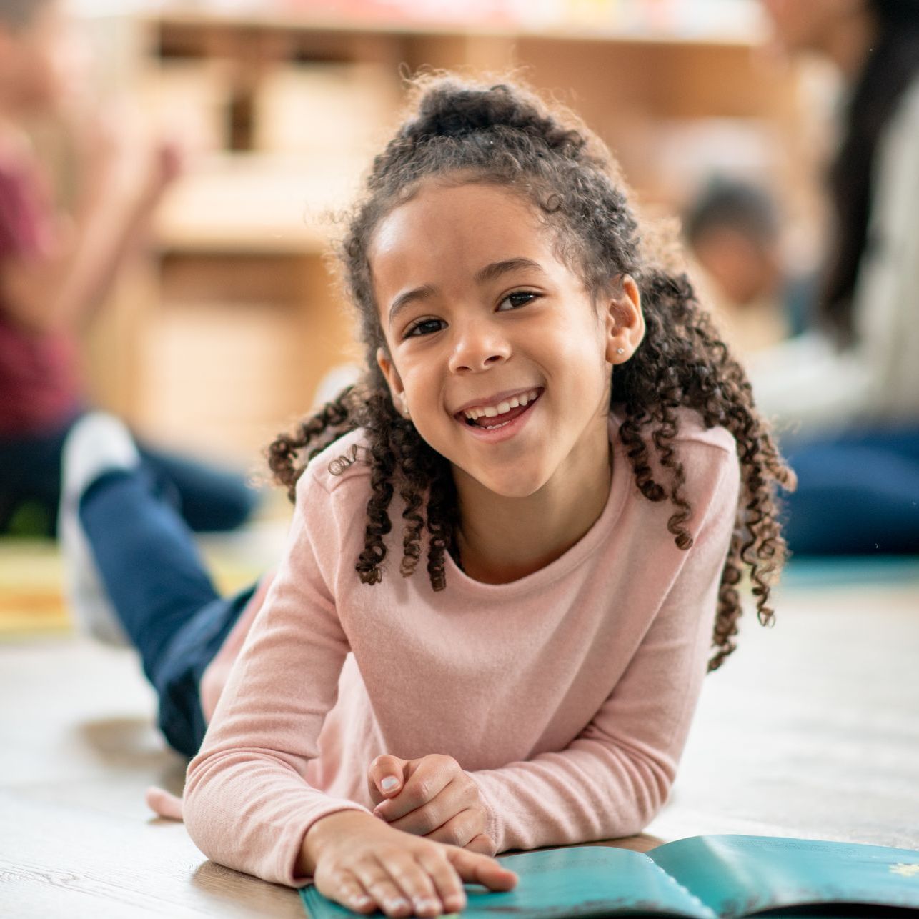 A little girl is laying on the floor reading a book and smiling.