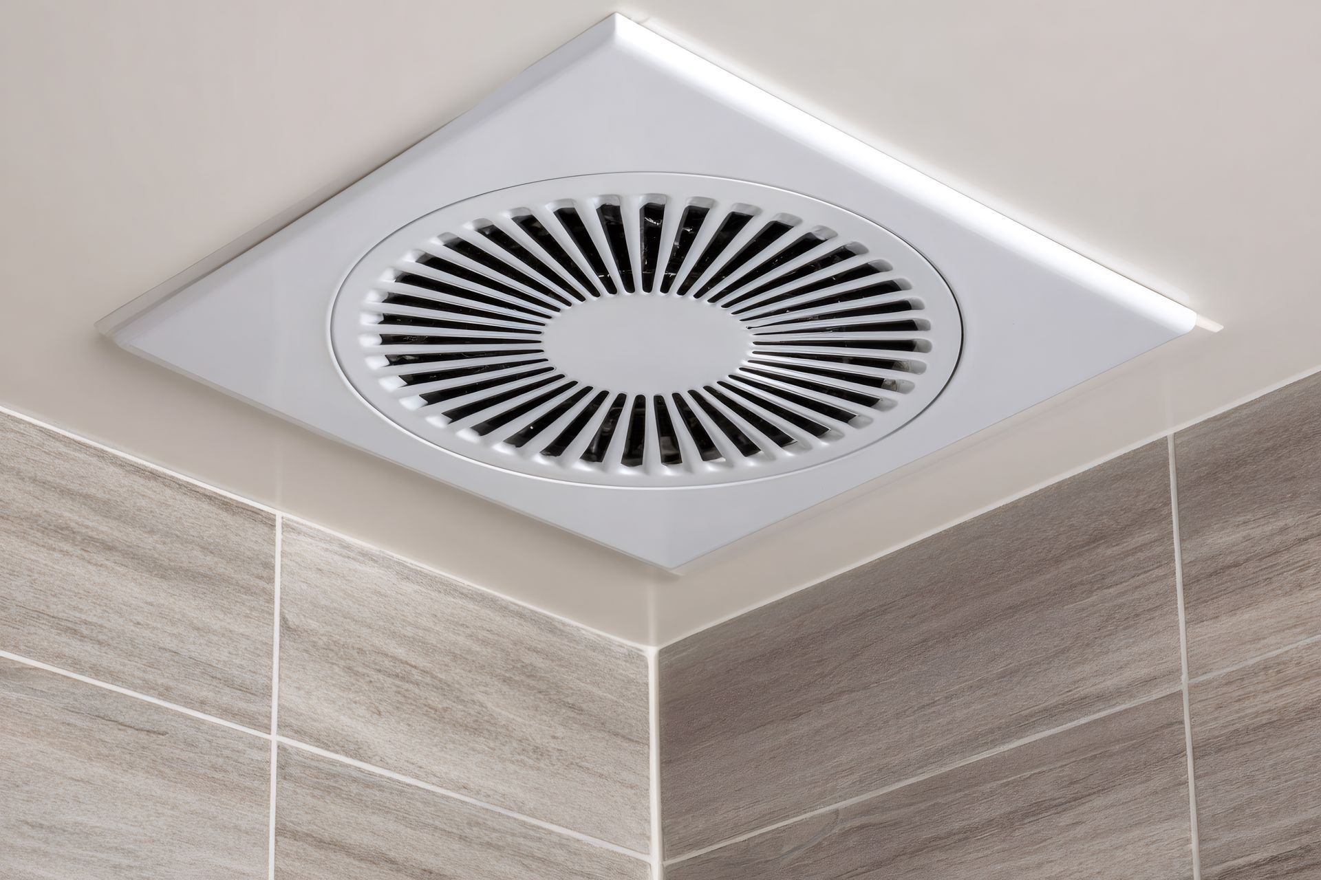 White ceiling exhaust fan in the corner of a tiled bathroom.