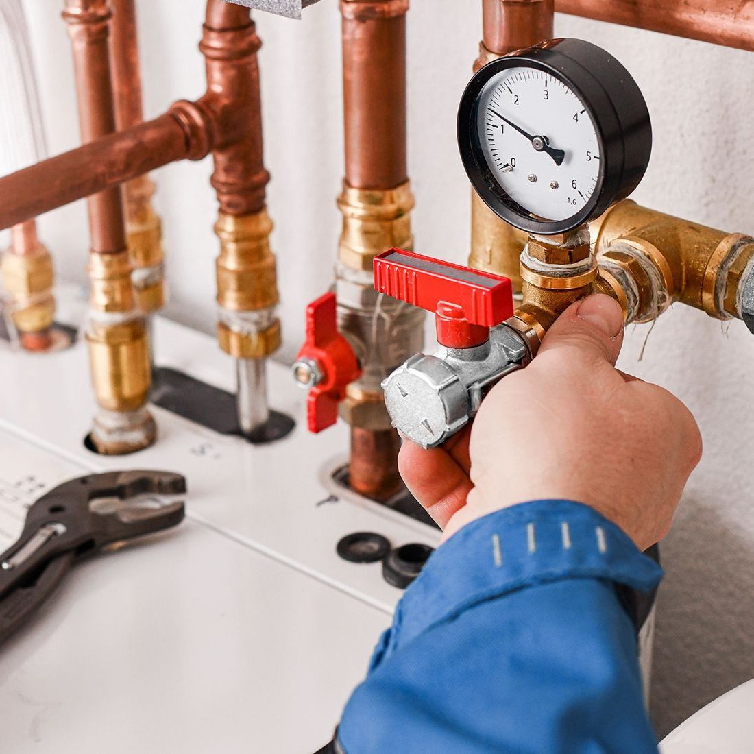 A person in a blue shirt adjusts a valve on copper pipes connected to a pressure gauge. A wrench rests nearby.