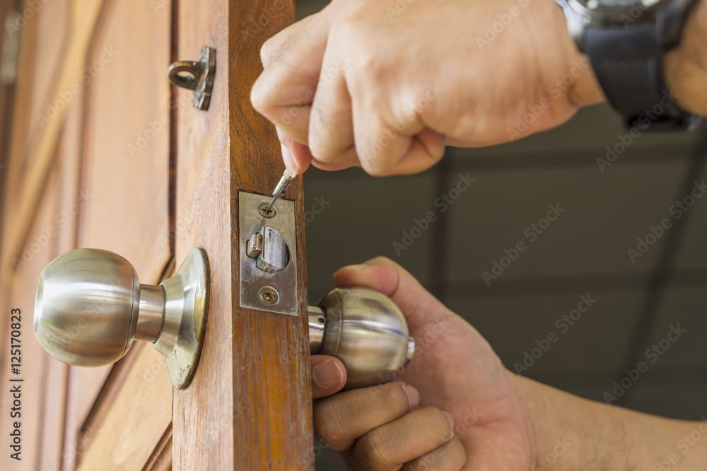 Hands using a key to unlock a silver doorknob on a wooden door.