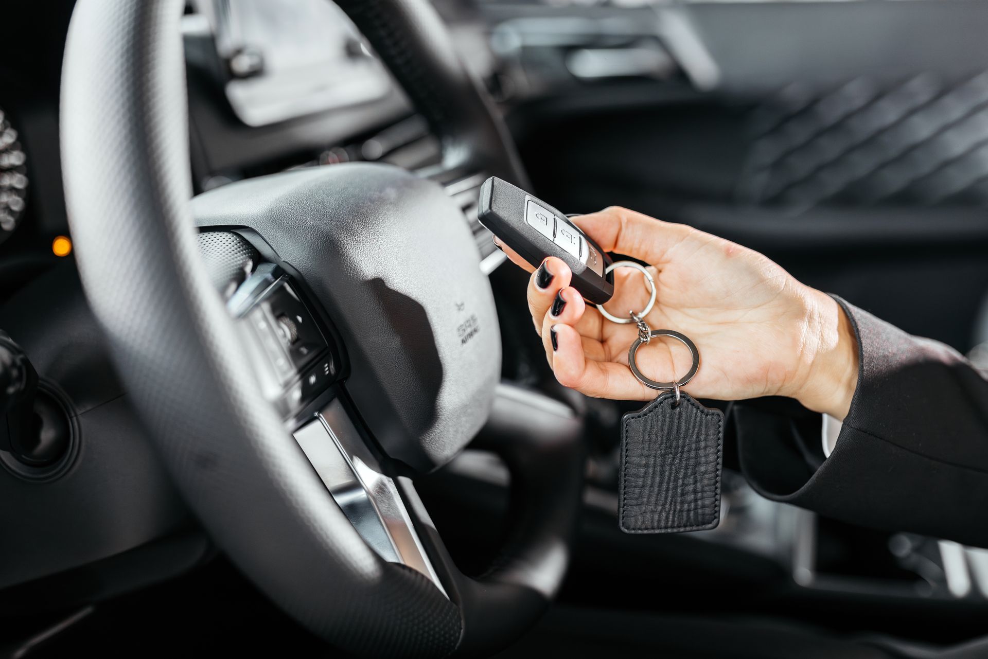 Woman in formal attire holding car key fob while sitting in modern vehicle.
