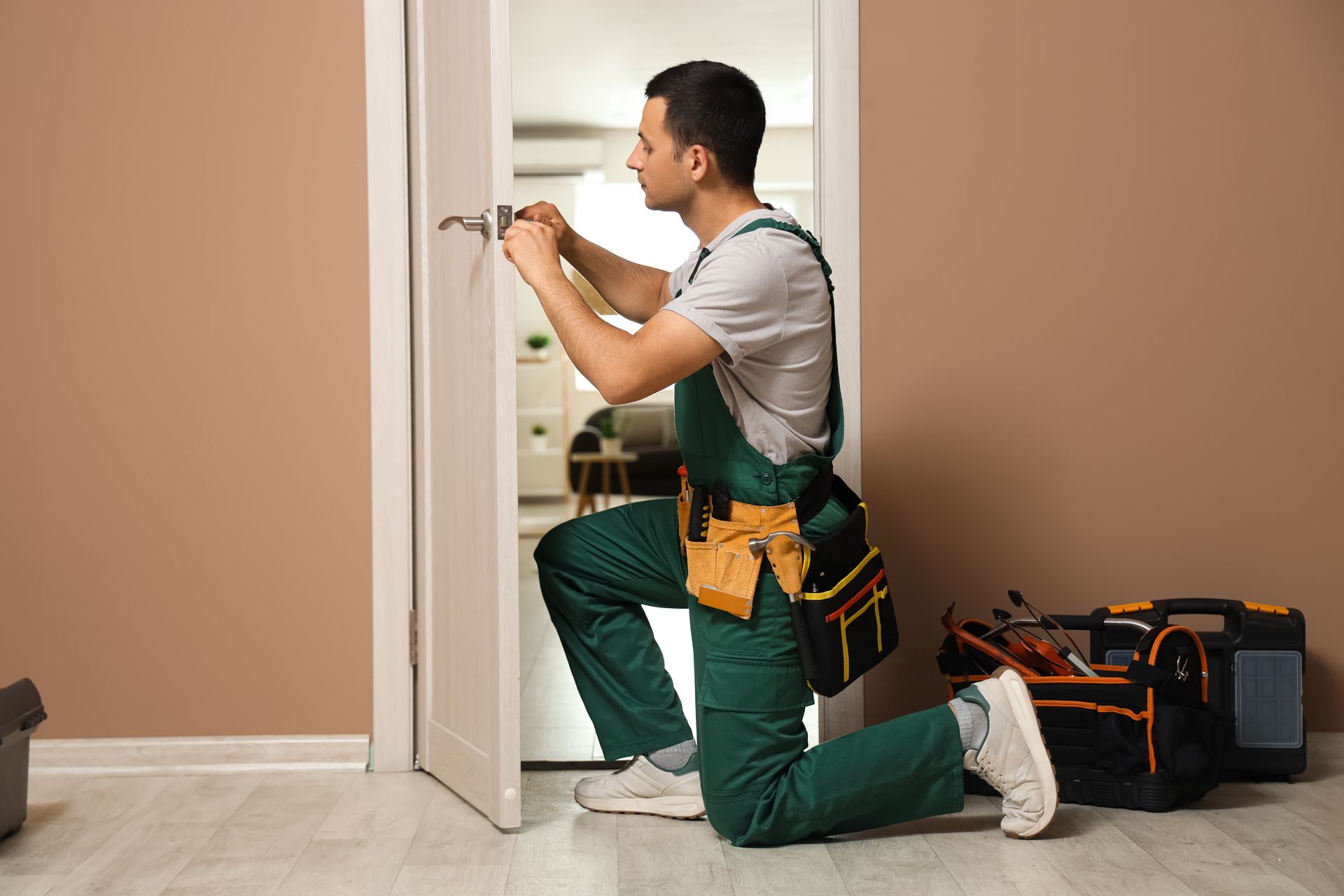 A residential locksmith wearing green overalls is using a screwdriver to repair a door at home.