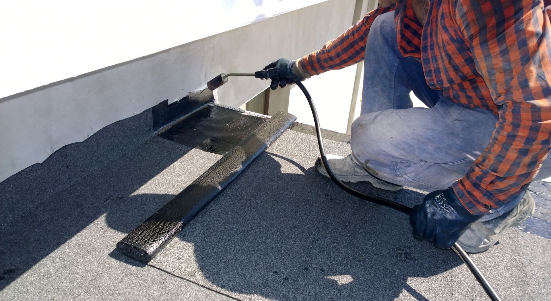 Worker applying roofing sealant with a trowel on a flat roof edge
