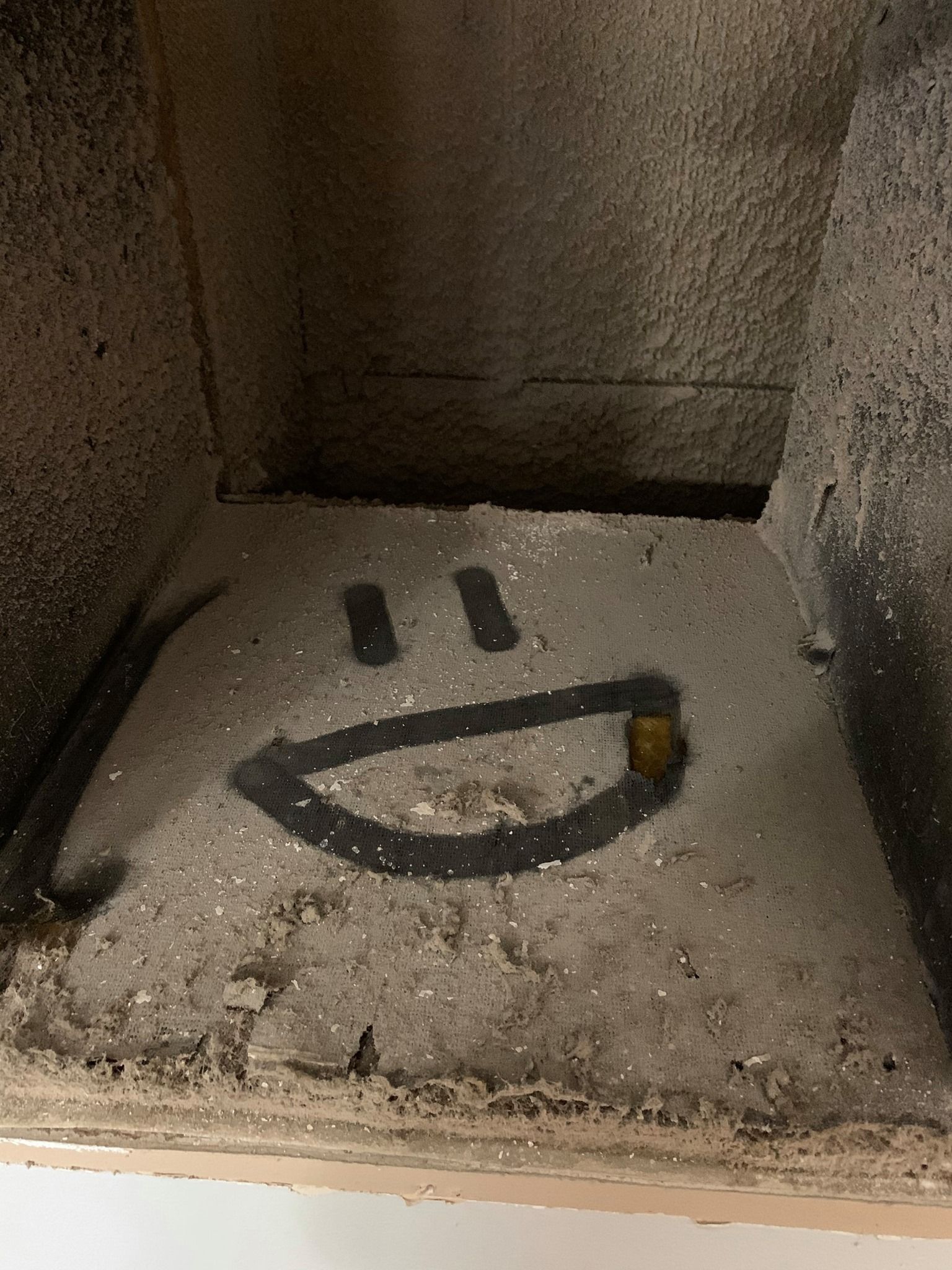 Smiley face graffiti drawn on a dusty surface within a dark enclosed space.
