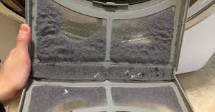 A hand holding a lint-filled dryer filter, grey lint against a grey filter.