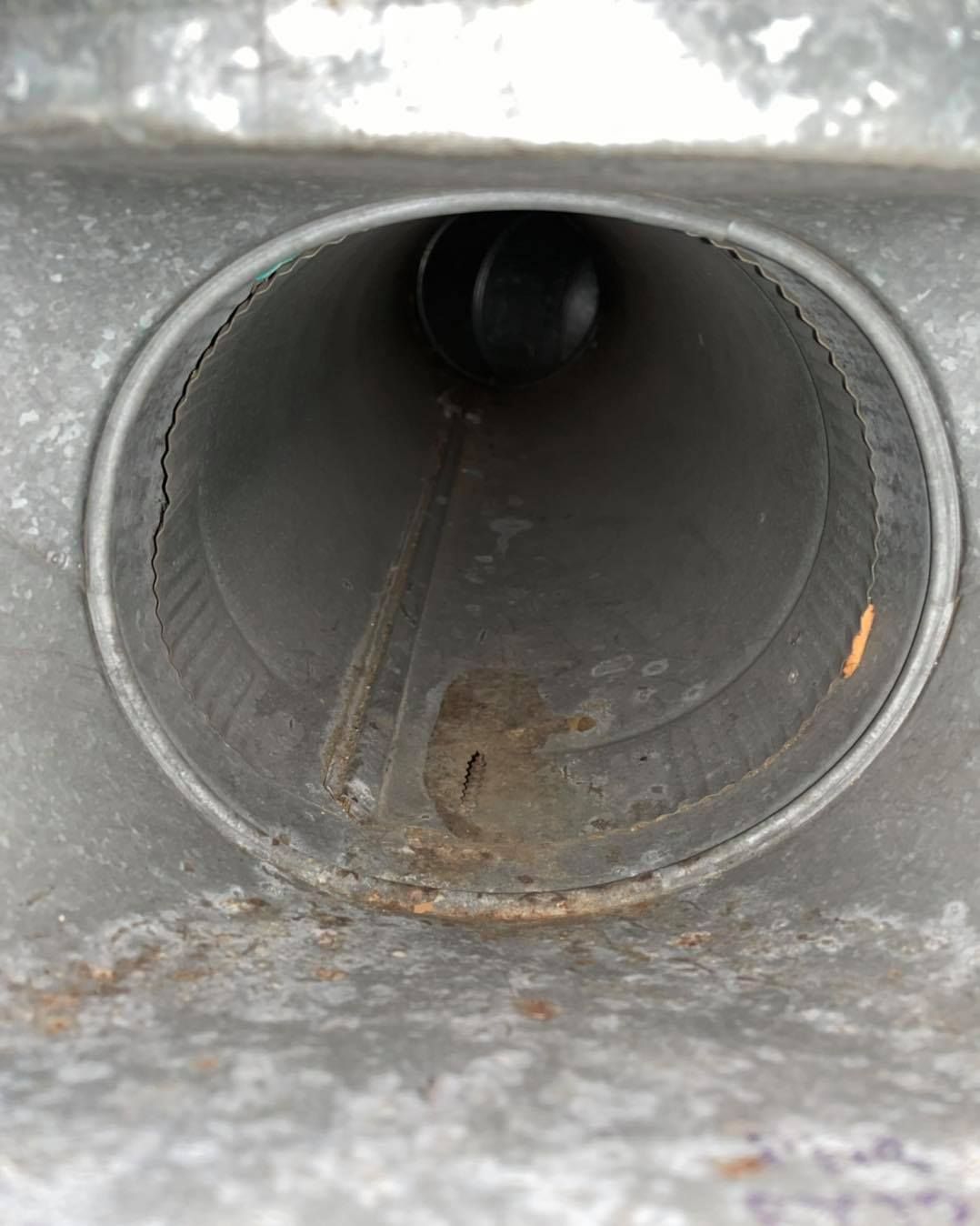 Close-up view of a rusted metal duct, circular with visible imperfections and a dark interior.