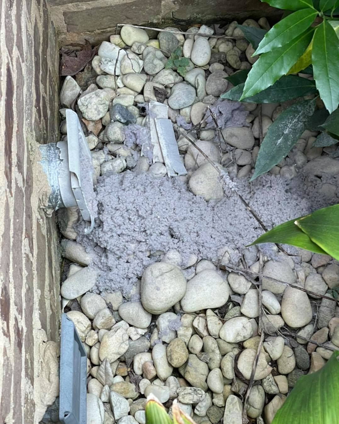 Gray debris pile on white pebbles near a brick wall and a metal vent.