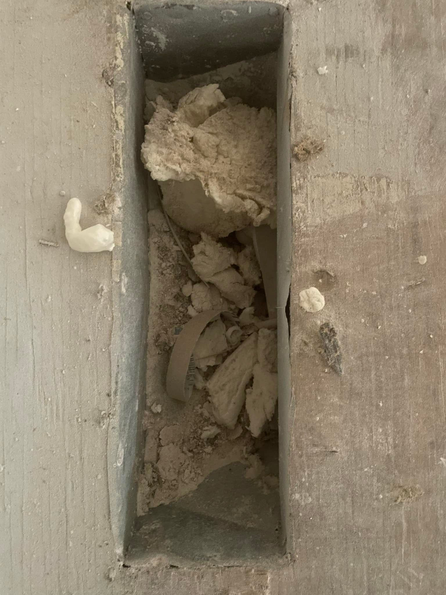 A rectangular recessed space in concrete filled with clumps of light-brown material, possibly mortar.