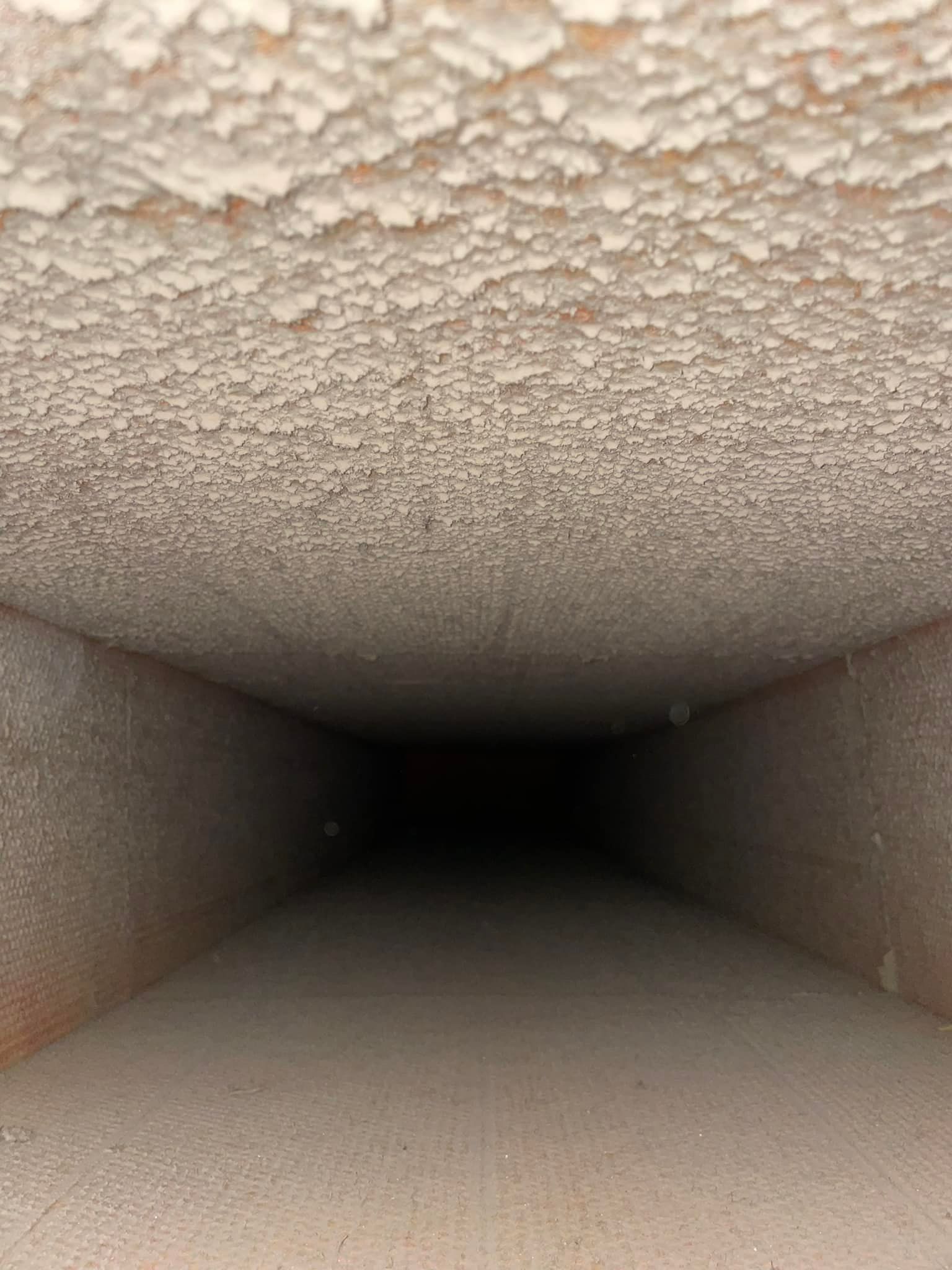 Interior of a rectangular air duct with white, textured buildup on the top.