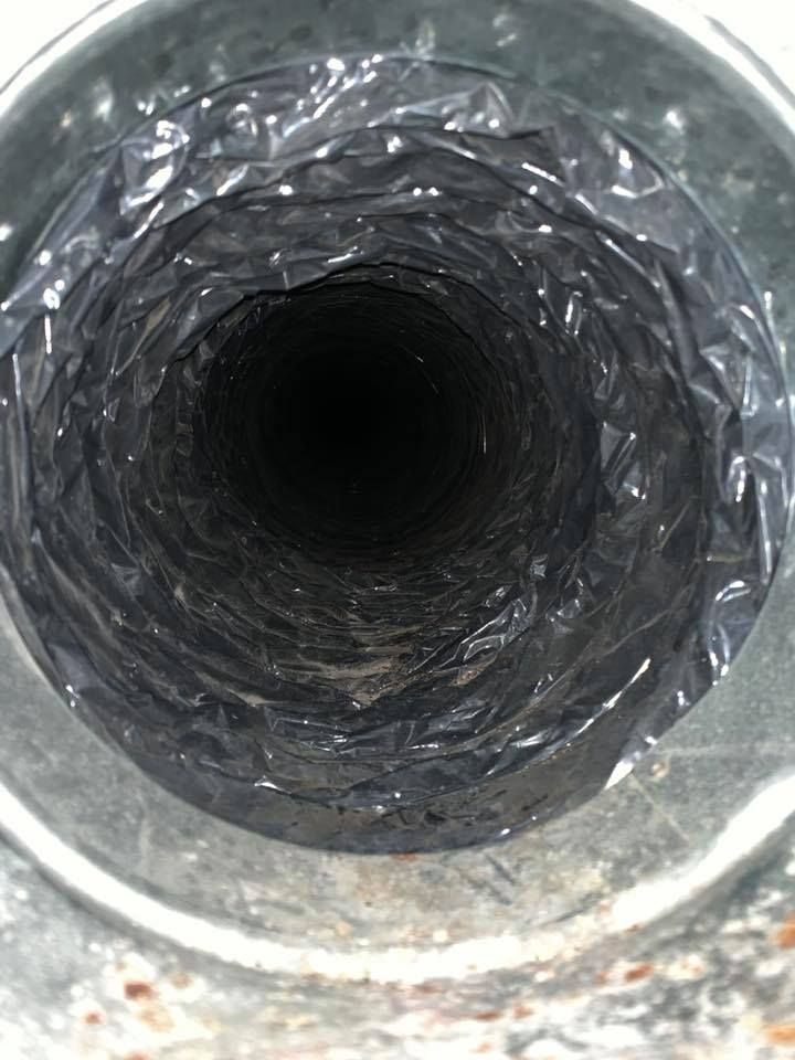 Inside view of a flexible, dark HVAC duct, with a corrugated, reflective interior, within a metal collar.