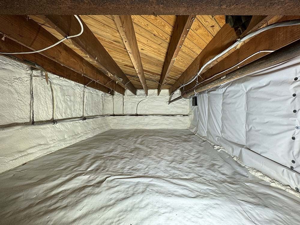 Crawl space with white insulation on walls and floor, wooden beams overhead.