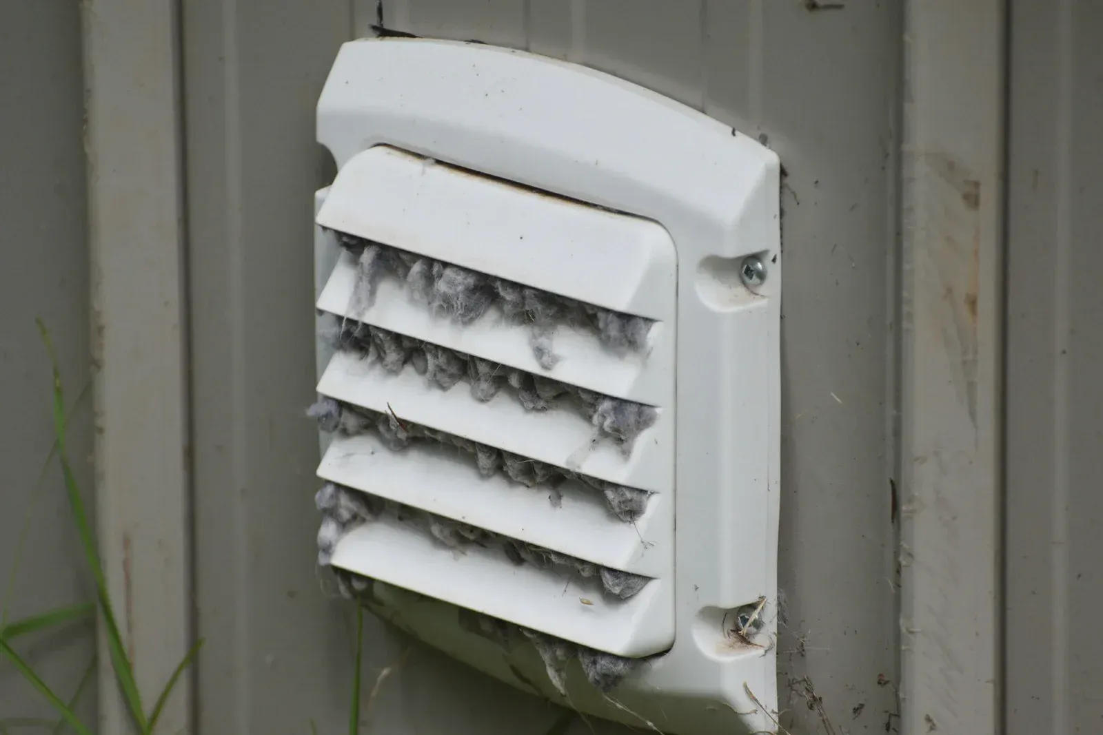 White plastic vent covered in gray debris on a gray wall.