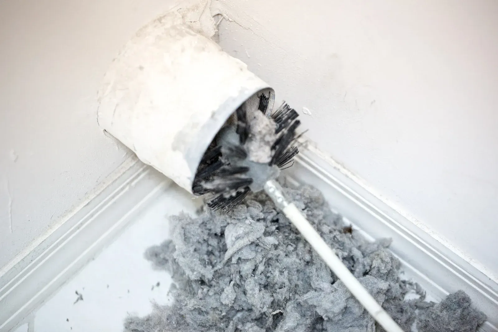 Cleaning a dryer vent with a brush, removing a large pile of lint from inside the vent.