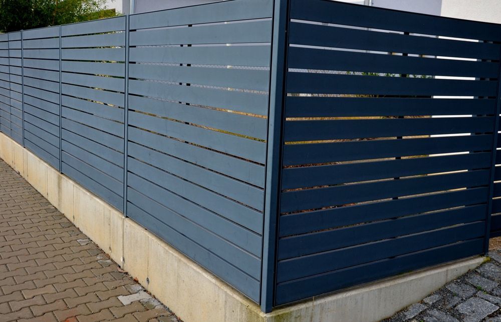 A Blue Wooden Fence is Sitting Next to a Brick Sidewalk — Harbour Fencing In Moonee Beach, NSW