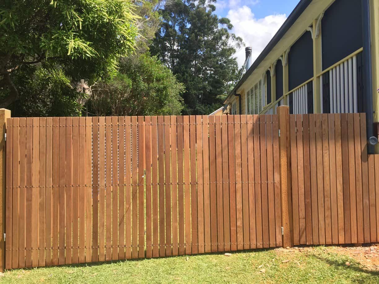 A Wooden Fence Surrounds a Lush Green Yard in Front of a House — Harbour Fencing In Moonee Beach, NSW