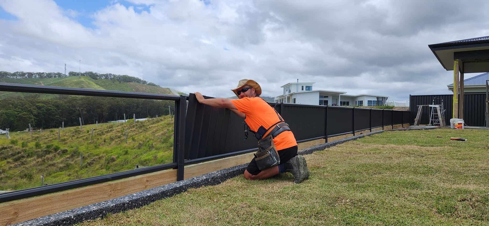 A Man is Kneeling Down in Front of a Fence — Harbour Fencing In Moonee Beach, NSW