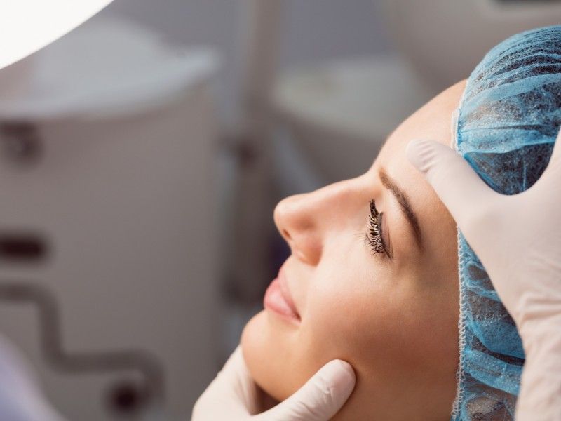 Uma mulher usando uma touca cirúrgica e luvas está recebendo um tratamento facial.