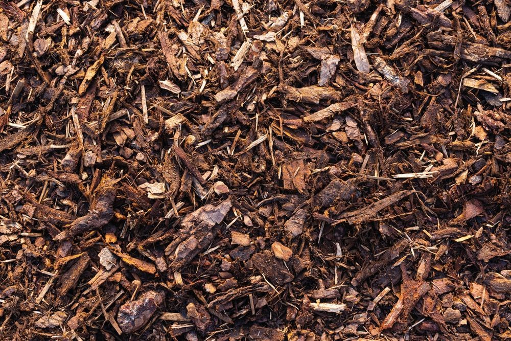 A top-down view of dark brown wood mulch pieces, showing various shapes, sizes, and textures.