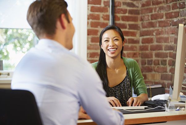 A man and a woman are sitting at a desk talking to each other.