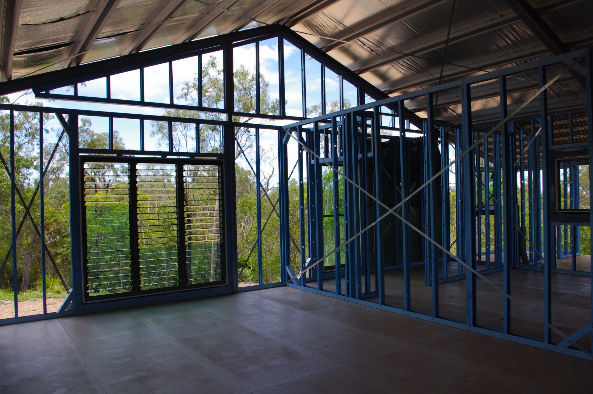 Interior view of a house under construction, with blue metal frame, windows, and a view of trees  — Steel Homes Australia in Branyan, QLD