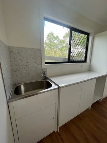 Laundry room with white cabinets, stainless steel sink, window, and tiled backsplash — Steel Homes Australia in Branyan, QLD